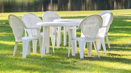 36305411 - white plastic table and chairs outside in a garden on green lawn by a pond or lake in the afternoon sun and a peaceful relaxing serene tranquil setting